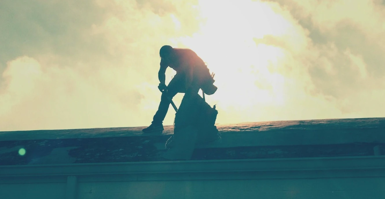 A roofer with a nail gun installing new shingles.